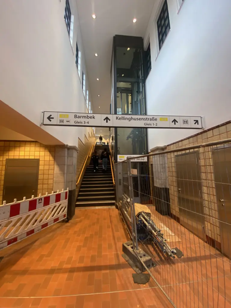 Vergleichbare Ansicht der Eingangshalle 2026, mit Treppe, Glasaufzug und Wegweisern