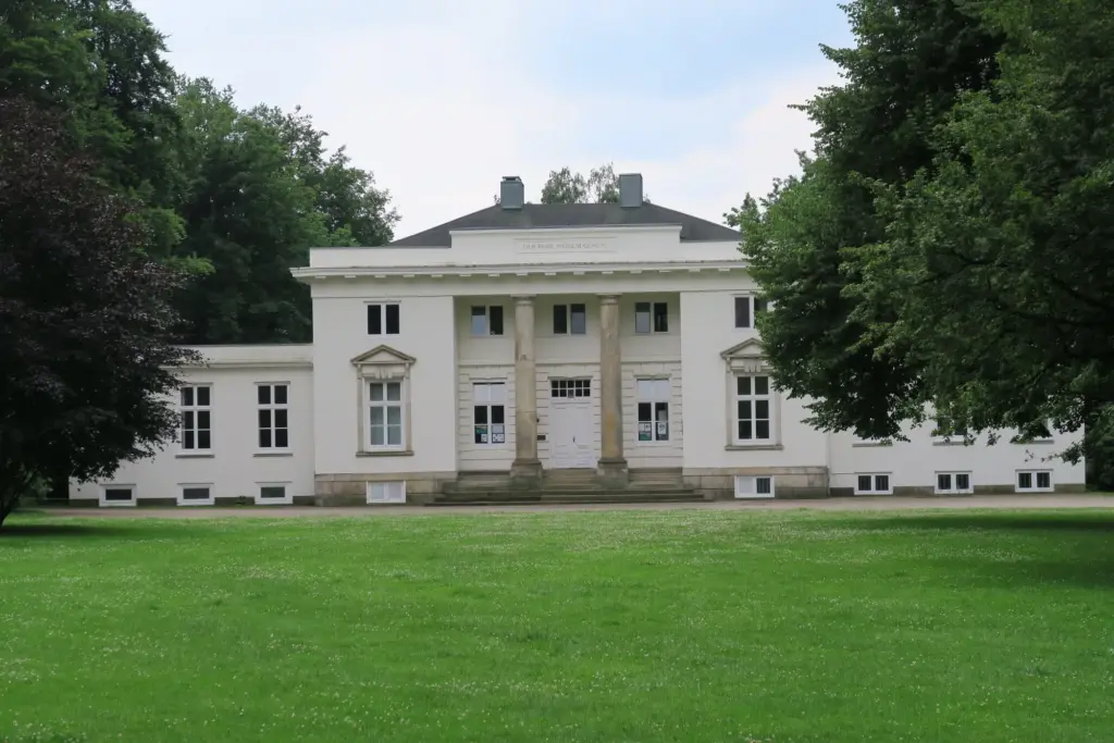 Klassizistisches weißes Landhaus mit Säulenportikus hinter einer Rasenfläche im Hirschpark