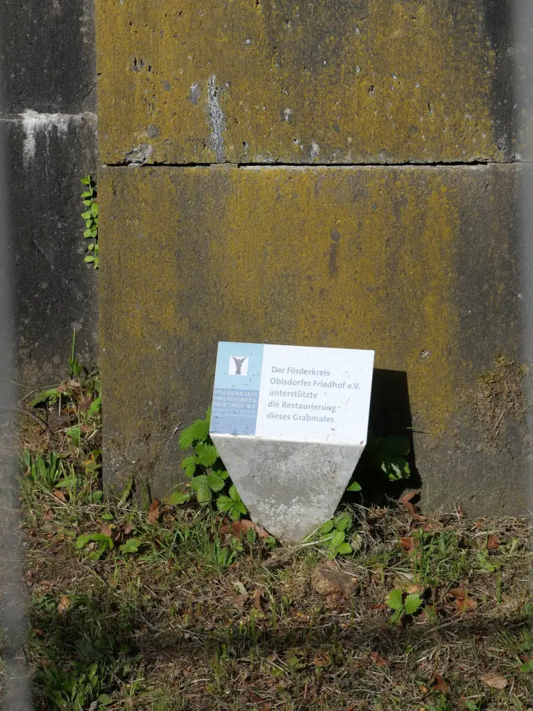 Kleiner heller Hinweisstein des Förderkreises Ohlsdorfer Friedhof am Sockel des Mausoleums, im Gras vor bemoostem Sandsteinquader