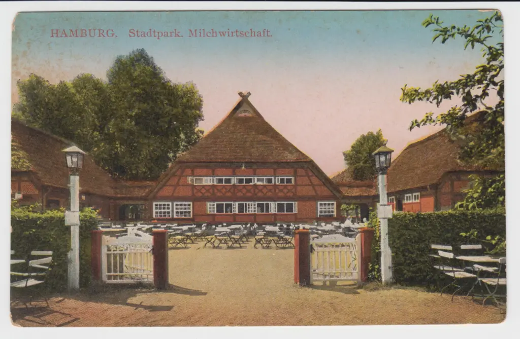 Die Milchwirtschaft im Hamburger Stadtpark auf einer kolorierten Postkarte: Fachwerkhaus mit Reetdach, davor der Hofplatz mit Gartenstühlen und das Tor zwischen zwei Laternenpfosten