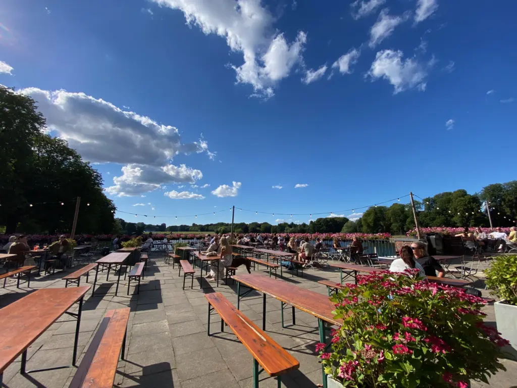 Biergarten mit Bierbänken auf einer Terrasse über dem Stadtparksee, im Hintergrund die Festwiese