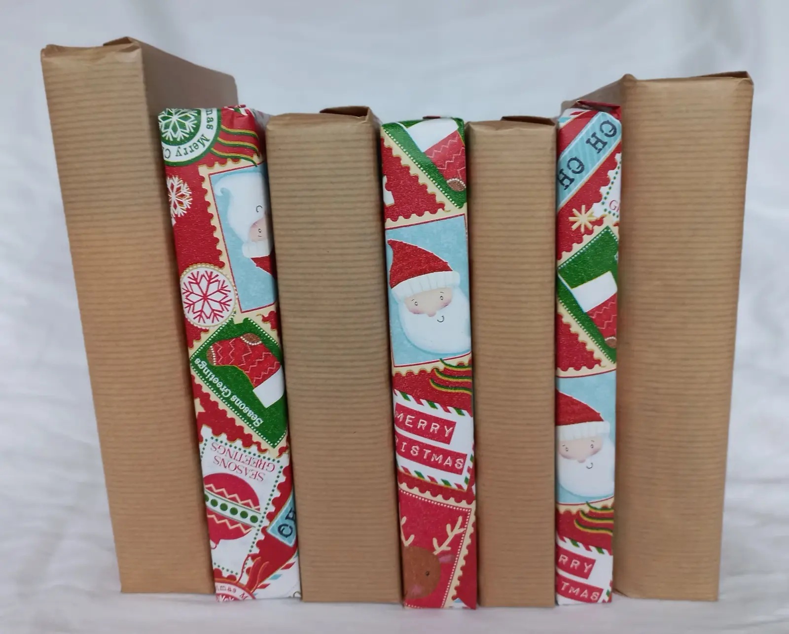 Sechs Bücher, abwechselnd in braunes Packpapier und Weihnachtspapier mit Weihnachtsmännern eingeschlagen, stehen nebeneinander.
